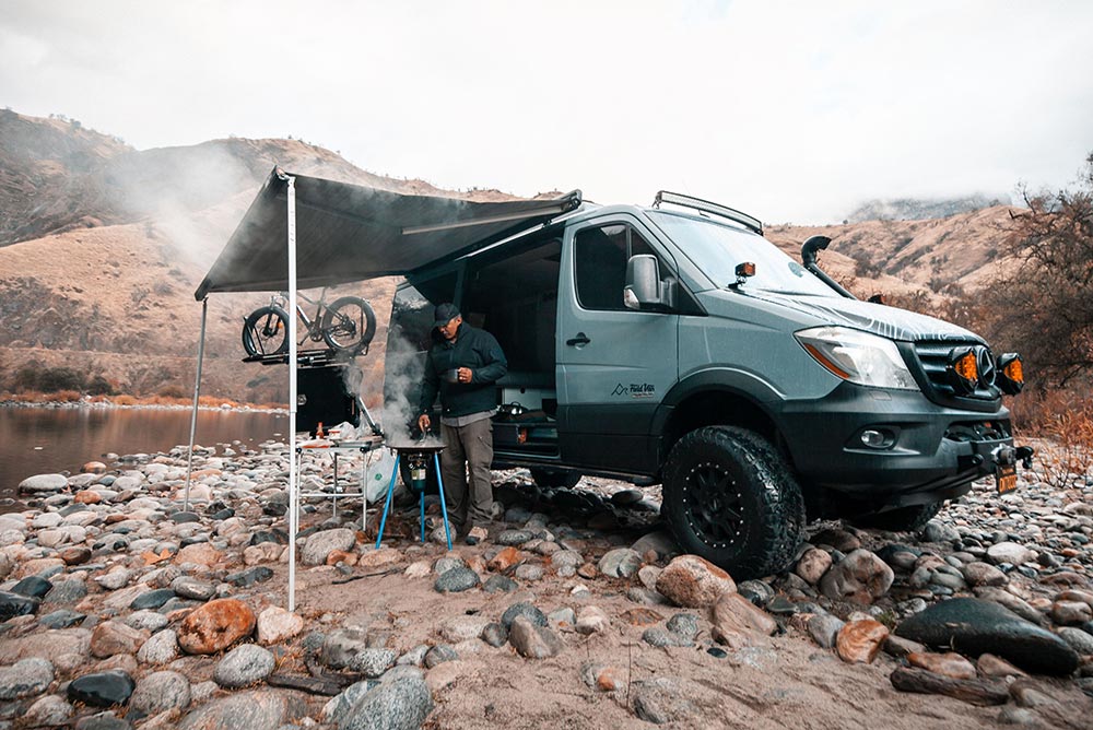 Man cooking in the backcountry next to a Field Van