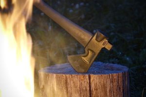 An axe resting in stump illuminated by a campfire.