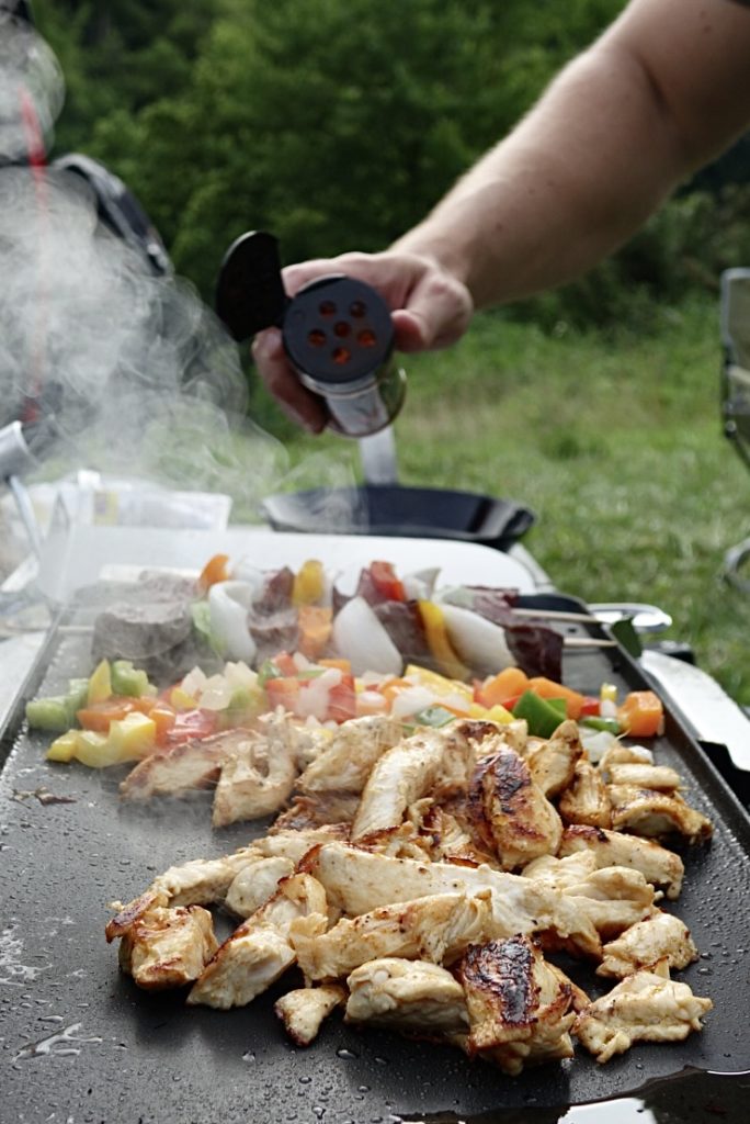 Steam rolling off of chicken and vegetables on a griddle.