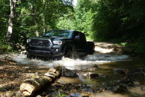 A Toyota Tacoma crossing a stream in the woods.