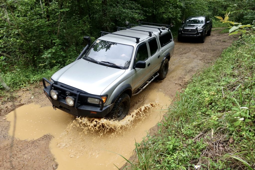 Two Toyota Tacomas on dirt road.