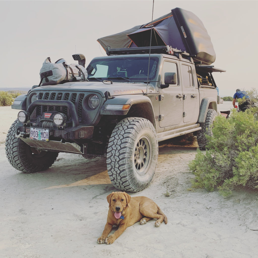Dog lies on the ground in front of a Jeep at camp