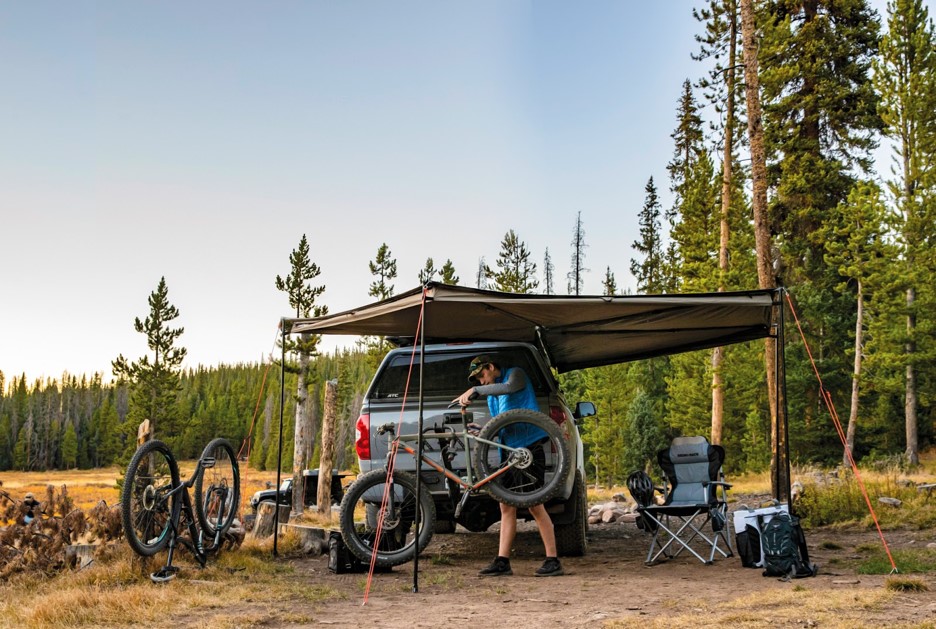 Man working on a bike under a RhinoRack Batwing awning.