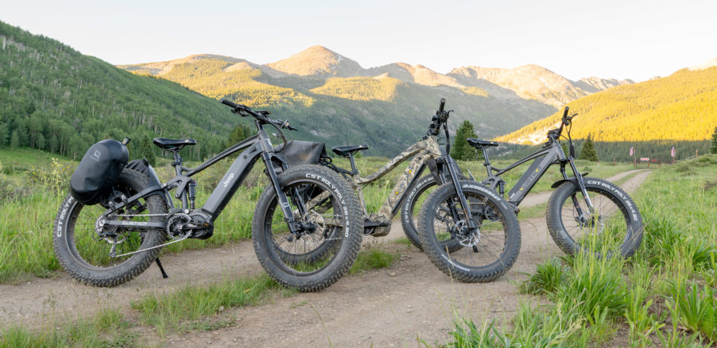 Three models of QuietKat electric mountain bikes lined up on a trail.