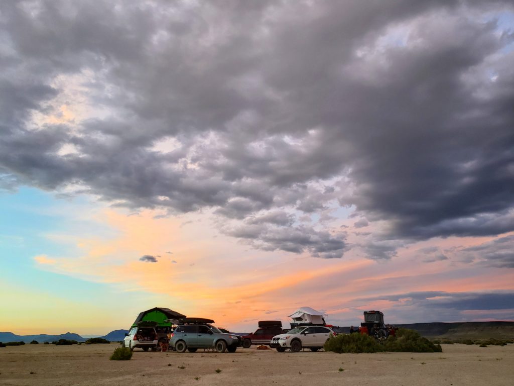 Subarus camped in the desert with pink clouds in the background.