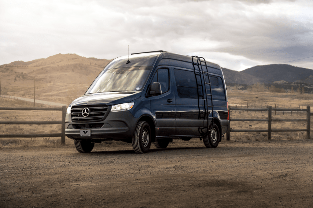 Shows a Mercedes Sprinter van in front of rolling hills.