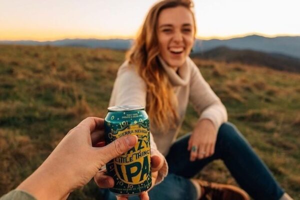 Someone hands a beer to a woman in a field