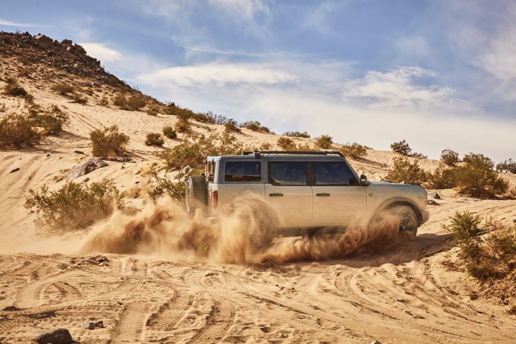 Ford Bronco throwing dirt as it speeds through the sand.