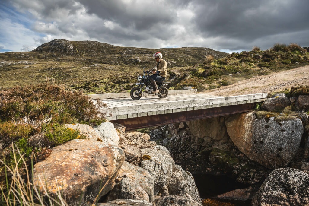 Man riding a Venturo motorcycle on an adventure over a bridge