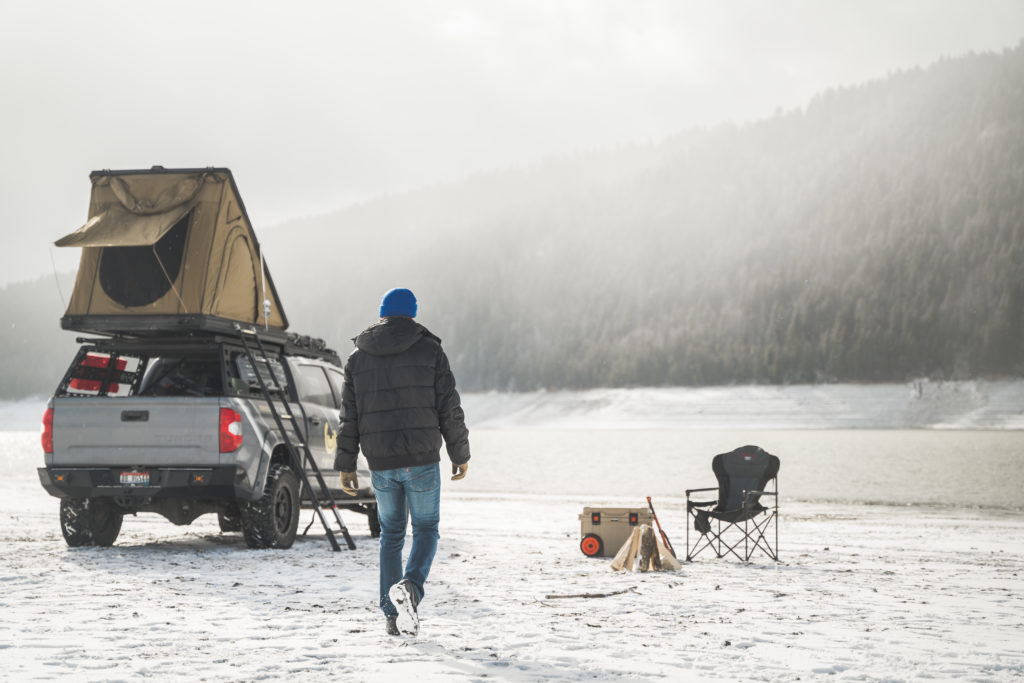 Man camping in the snow with a rooftop tent on a Toyota Tundra.