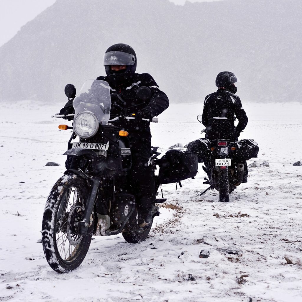 Two riders on Royal Enfield Himalayans riding in the snow