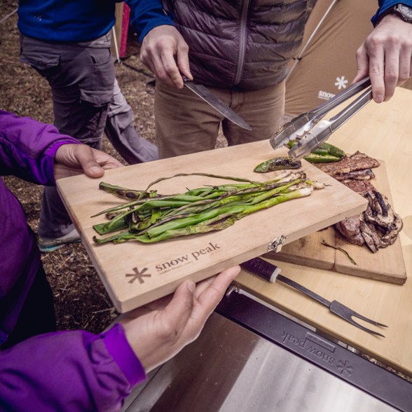 People using the Snow Peak Cutting Board and Knife Set to chop vegetables in the outdoors.