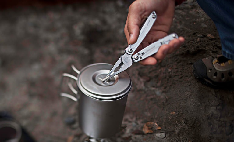 Using a Leatherman multitool to remove a hot lid from a cookstove in the backcountry.