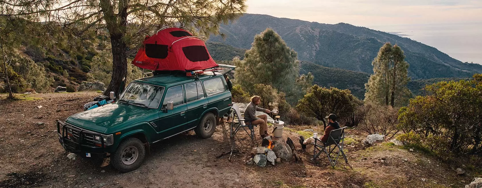 People at camp overlooking a forest at the top of a mountain trail.