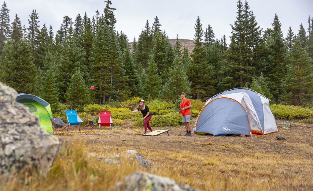 Two people at camp playing cornhole with Big Agnes chairs and tents.