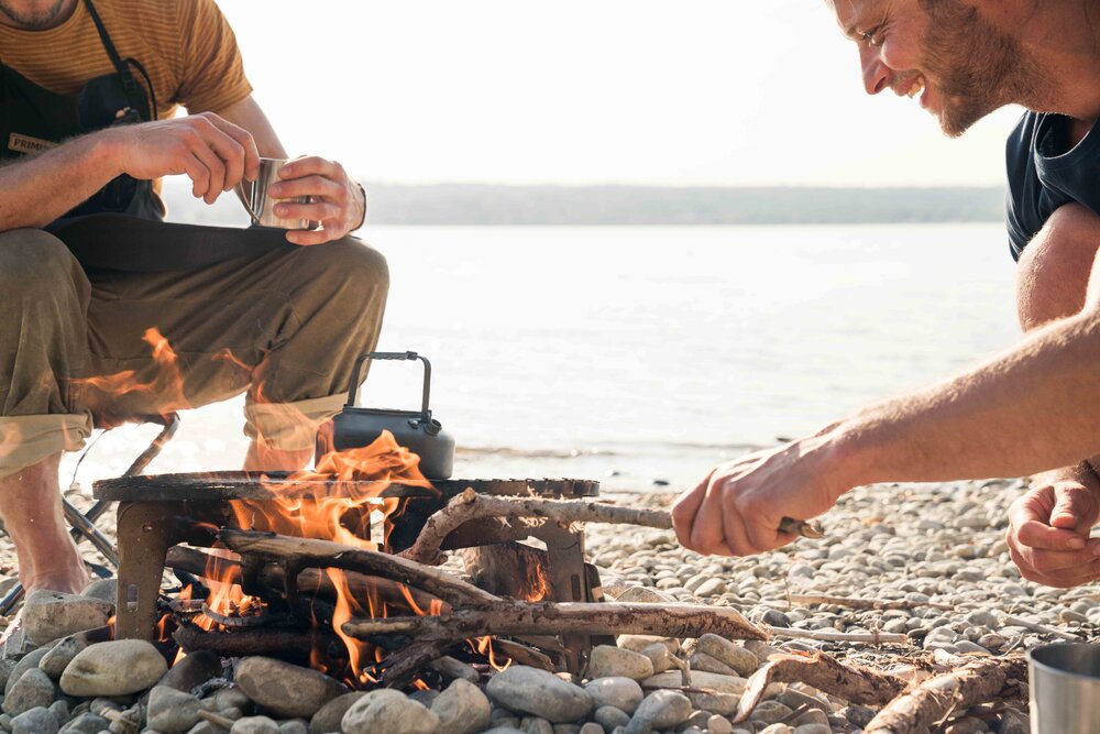 Two campers cooking over and open fire on the beach with the Primus Aeril Stove.