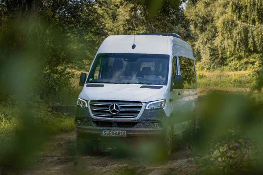 Mercedes-Benz Sprinter driving through the forest on a dirt road.