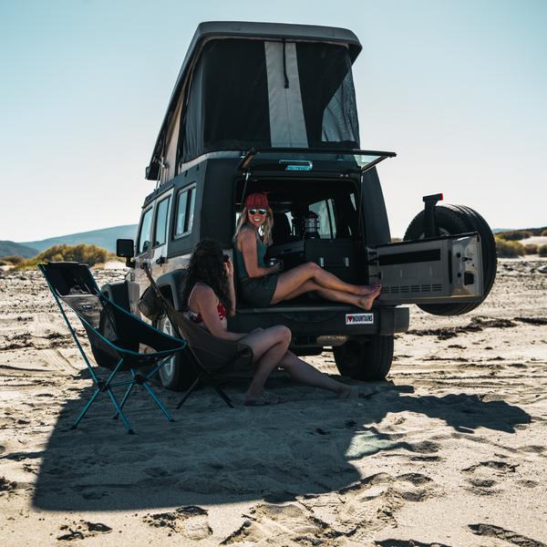 Two women relaxing at a beach camp with their Helinox Sunset Chairs.