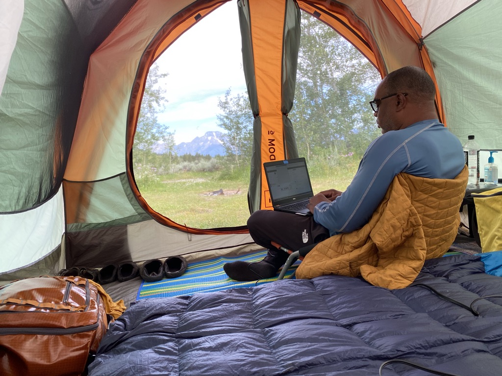 Digital nomads can work anywhere. Man working in a tent in the mountains.