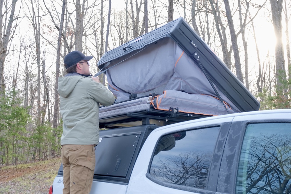 A man closing a rooftop tent on top of a truck. 