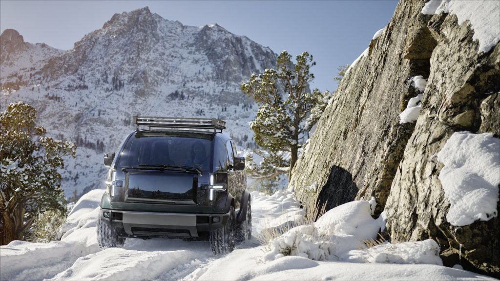 Canoo Pickup driving through snow on a mountain trail.