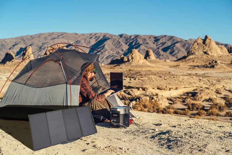 Man using EcoFlow 160W Solar Panel to power his computer in a ground tent in the desert.