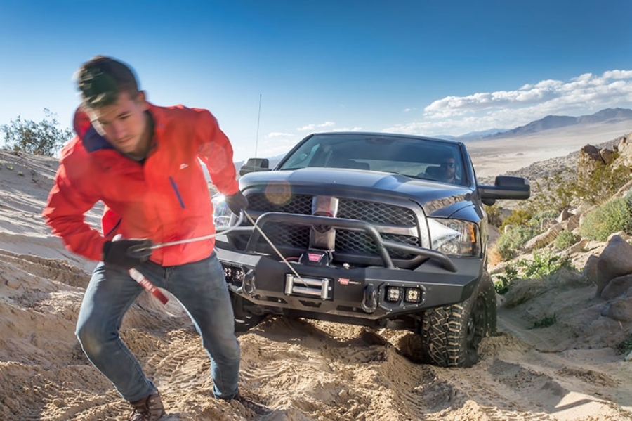 Man spooling out a winch line on a truck to attach to an anchor point.