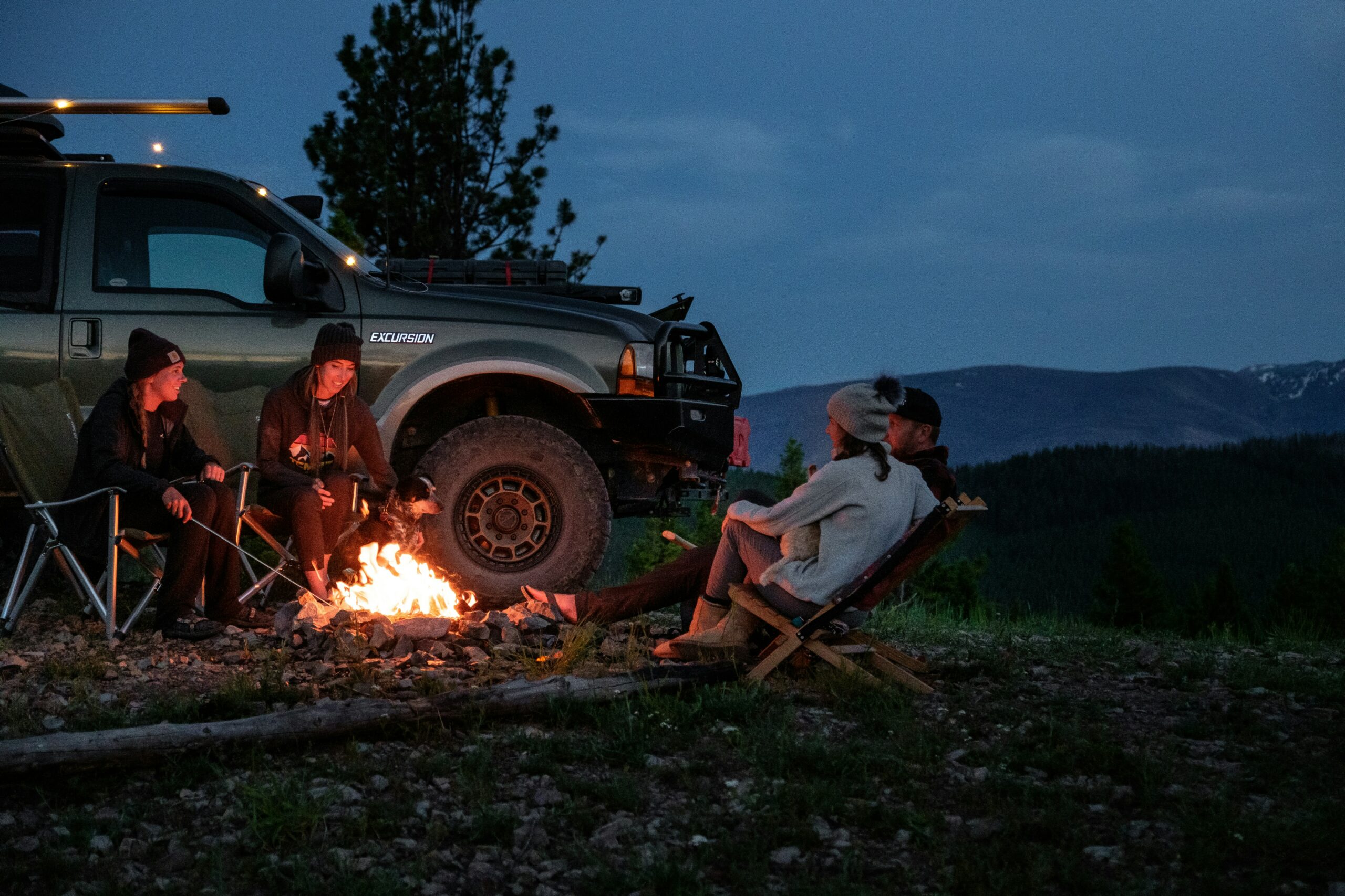 group of campers gathered arounda. campfire with a truck in the background